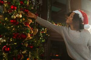 Merry Christmas. African American woman decorating Christmas tree. Happy girl near traditional Christmas tree with classical red golden decorations ornament, Christmas eve at home time for celebration photo