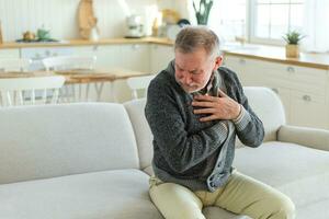 Pain on heart, heart attack. Unhappy middle aged senior man suffering from chest pain heart attack problems with health at home. Mature old senior grandfather touching chest experiencing infarction. photo