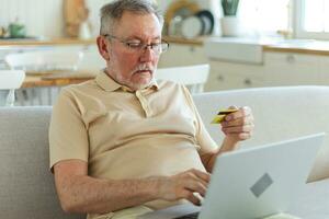 Senior man shopping online using laptop paying with credit card. Old grandfather buying on Internet enter credit card details. Online shopping delivery service. Older generation modern tech usage. photo