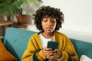 African girl holding smartphone touch screen typing scroll page at home. Woman with cell phone surfing internet using social media apps playing game. Shopping online Internet news cellphone addiction. photo