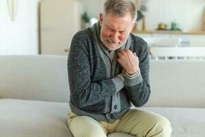 Pain on heart, heart attack. Unhappy middle aged senior man suffering from chest pain heart attack problems with health at home. Mature old senior grandfather touching chest experiencing infarction. photo