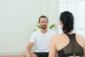 Young female and male athletes sitting rest on yoga mats and drinking water. They are looking at each other and smiling photo