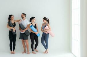 A group of female and male athletes stood and chatted amicably in the studio before beginning with the yoga class. photo