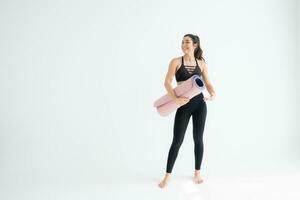 Full length portrait of a young woman holding yoga mat isolated on white background photo