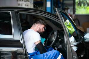 A young man vehicle technician working inside a car at an auto repair shop. photo