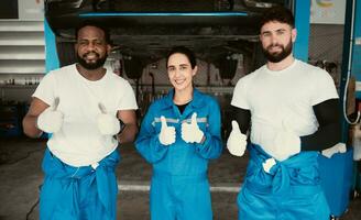 Portrait of smiling mechanics standing in auto repair shop and showing thumbs up photo