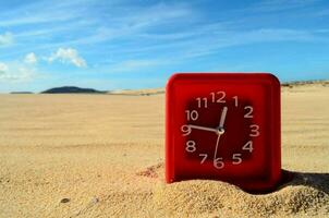 a red clock sitting in the sand on a beach photo