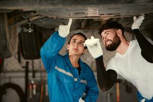 ambos de coche mecánico trabajando en un auto reparar comercio, cheque el operación de el motor de debajo el coche ese viene en para refacción a el auto reparar tienda. foto