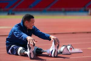 discapacitado atlético hombre extensión y calentamiento arriba antes de corriendo en estadio pista foto