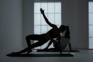 Silhouette of a young couple practicing yoga in the room. photo