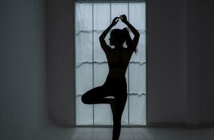silueta de un joven mujer practicando yoga en el habitación. foto