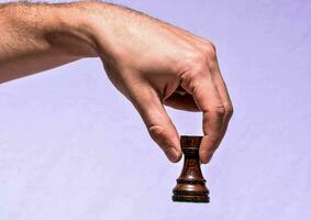 a hand holding a wooden chess piece on a purple background photo