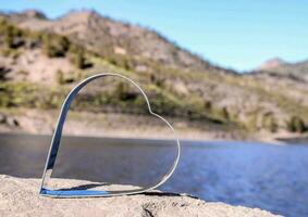 a heart shaped metal object sitting on a rock by a lake photo