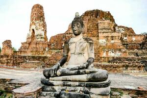 un budista estatua se sienta en frente de un arruinado templo foto