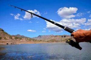 a person holding a fishing rod in front of a lake photo