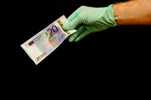 a person in a green glove holding a twenty euro bank note photo