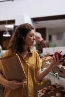 Woman in zero waste shop purchasing farm grown vegetables, picking ripe bell peppers. Client in plastic free local grocery shop looking to buy nutritious food, using decomposable paper bag photo