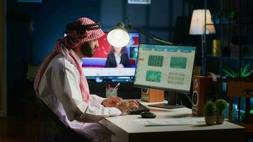 Arabic broker investor in home office checking stock exchange valuation, writing down investment financial profit figures. Middle Eastern stockholder looking at market shares growth charts on digital video