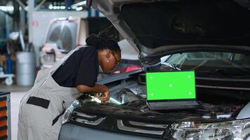 cerca arriba Disparo de ordenador portátil metido en abrió arriba coche en ocupado garaje mientras africano americano técnico arregla vehículo. Bosquejo dispositivo en reparar tienda con calificado empleado trabajando siguiente a eso foto