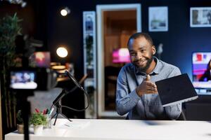 African american internet show host using professional camera and microphone to film content about best gaming laptops of the year. Tech engineer recording notebook digital device review photo