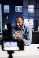 Focus on african american content creator filming tech reviews for his internet channel, using professional video production gear in blurry background used for capturing footage photo