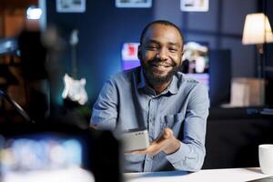 African american audio engineer assessing portable speaker, showing dissatisfaction with subpar materials used. Internet show host displeased with low quality wireless music playing device photo