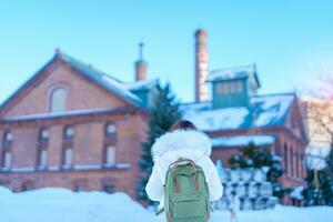 Woman tourist Visiting in Sapporo, Traveler in Sweater looking Sapporo Beer Museum with Snow in winter season. landmark and popular for attractions in Hokkaido, Japan. Travel and Vacation concept photo
