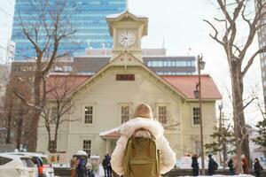 Woman tourist Visiting in Sapporo, Traveler in Sweater sightseeing Sapporo Clock tower with Snow in winter. landmark and popular for attractions in Hokkaido, Japan. Travel and Vacation concept photo