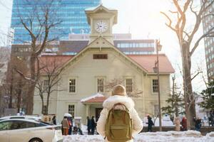 Woman tourist Visiting in Sapporo, Traveler in Sweater sightseeing Sapporo Clock tower with Snow in winter. landmark and popular for attractions in Hokkaido, Japan. Travel and Vacation concept photo