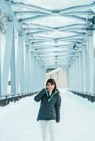 Woman tourist Visiting in Biei, Traveler in Sweater sightseeing Shirahige Waterfall bridge with Snow in winter. landmark and popular for attractions in Hokkaido, Japan. Travel and Vacation concept photo