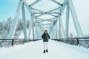 Woman tourist Visiting in Biei, Traveler in Sweater sightseeing Shirahige Waterfall bridge with Snow in winter. landmark and popular for attractions in Hokkaido, Japan. Travel and Vacation concept photo