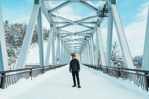 man tourist Visiting in Biei, Traveler in Sweater sightseeing Shirahige Waterfall bridge with Snow in winter. landmark and popular for attractions in Hokkaido, Japan. Travel and Vacation concept photo