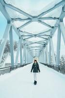 Woman tourist Visiting in Biei, Traveler in Sweater sightseeing Shirahige Waterfall bridge with Snow in winter. landmark and popular for attractions in Hokkaido, Japan. Travel and Vacation concept photo