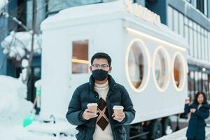 hombre turista participación caliente café o té papel taza con nieve en invierno temporada durante viaje en niseko. punto de referencia y popular para atracciones en Hokkaidō, Japón. viaje y vacaciones conceptos foto