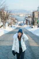 mujer turista visitando en hakodate, viajero en suéter Turismo hachiman zaka Pendiente con nieve en invierno. punto de referencia y popular para atracciones en Hokkaidō, Japón. viaje y vacaciones concepto foto