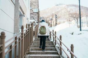 Woman tourist Visiting in Hakodate, Traveler in Sweater sightseeing Hachiman Zaka Slope with Snow in winter. landmark and popular for attractions in Hokkaido, Japan. Travel and Vacation concept photo