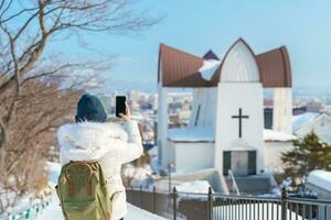 mujer turista visitando en hakodate, viajero en suéter Turismo episcopal Iglesia con nieve en invierno. punto de referencia y popular para atracciones en Hokkaidō, Japón. viaje y vacaciones concepto foto