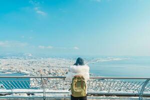 Woman tourist Visiting in Hakodate, Traveler in Sweater sightseeing view from Hakodate mountain with Snow in winter. landmark and popular for attractions in Hokkaido, Japan.Travel and Vacation concept photo