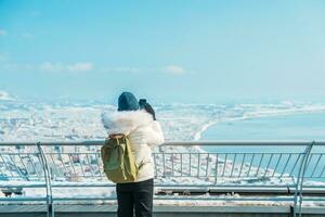 mujer turista visitando en hakodate, viajero en suéter Turismo ver desde hakodate montaña con nieve en invierno. punto de referencia y popular para atracciones en Hokkaidō, japon.viajes y vacaciones concepto foto