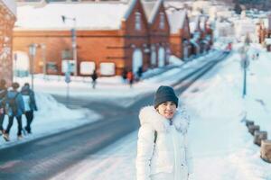 mujer turista visitando en hakodate, viajero en suéter Turismo kanemori rojo ladrillo almacén con nieve en invierno. punto de referencia y popular para atracciones en hokkaido, japón.travel y vacaciones concepto foto