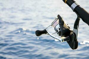 close up spinning fishing rod against blue sea watger background photo