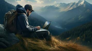 Hiker with backpack sitting on top of the mountain and using laptop photo