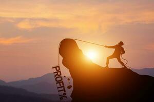 Silhouette of businessman pulling a profit rope with percentage in frame on a mountain with sunset background. concept of Business competition, financial crisis, loss, and investment risks photo