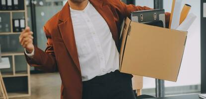 Business man employee stressful resignation from job while picking up personal belongings into brown cardboard box and carrying to walking out from office photo
