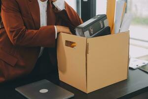 Business man employee stressful resignation from job while picking up personal belongings into brown cardboard box and carrying to walking out from office photo