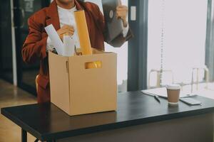 Business man employee stressful resignation from job while picking up personal belongings into brown cardboard box and carrying to walking out from office photo