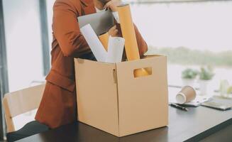 Business man employee stressful resignation from job while picking up personal belongings into brown cardboard box and carrying to walking out from office photo