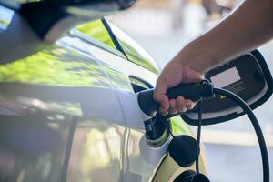 Man put plugs charging cable electric vehicle. Driver removes charger of his electric vehicle. photo