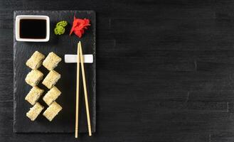 Sushi roll Philadelphia with salmon, sesame seeds, avocado, cream cheese on black slate background photo