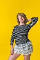 Cheerful blondie woman 49 years in mini skirt, striped T-shirt posing with hand behind head, smiling photo